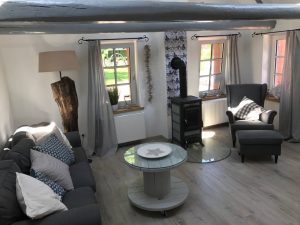 Graue Couch, Holzfußboden, Beistelltisch, Kaminofen, Ohrensessel, heller Raum